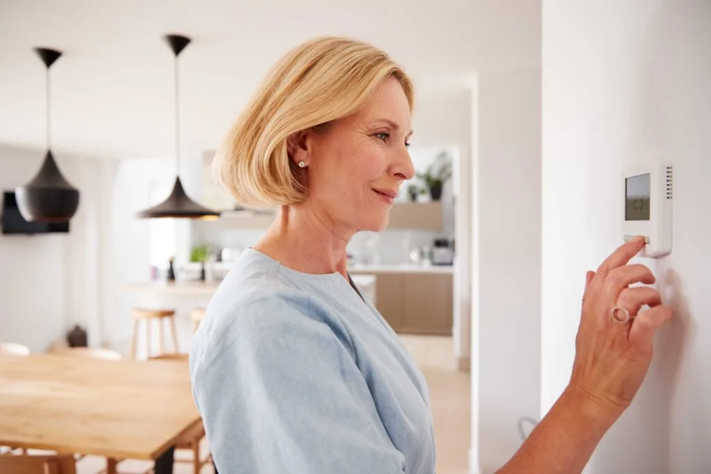 How to check the boiler   Lady changing her heating thermostat on the wall of her home